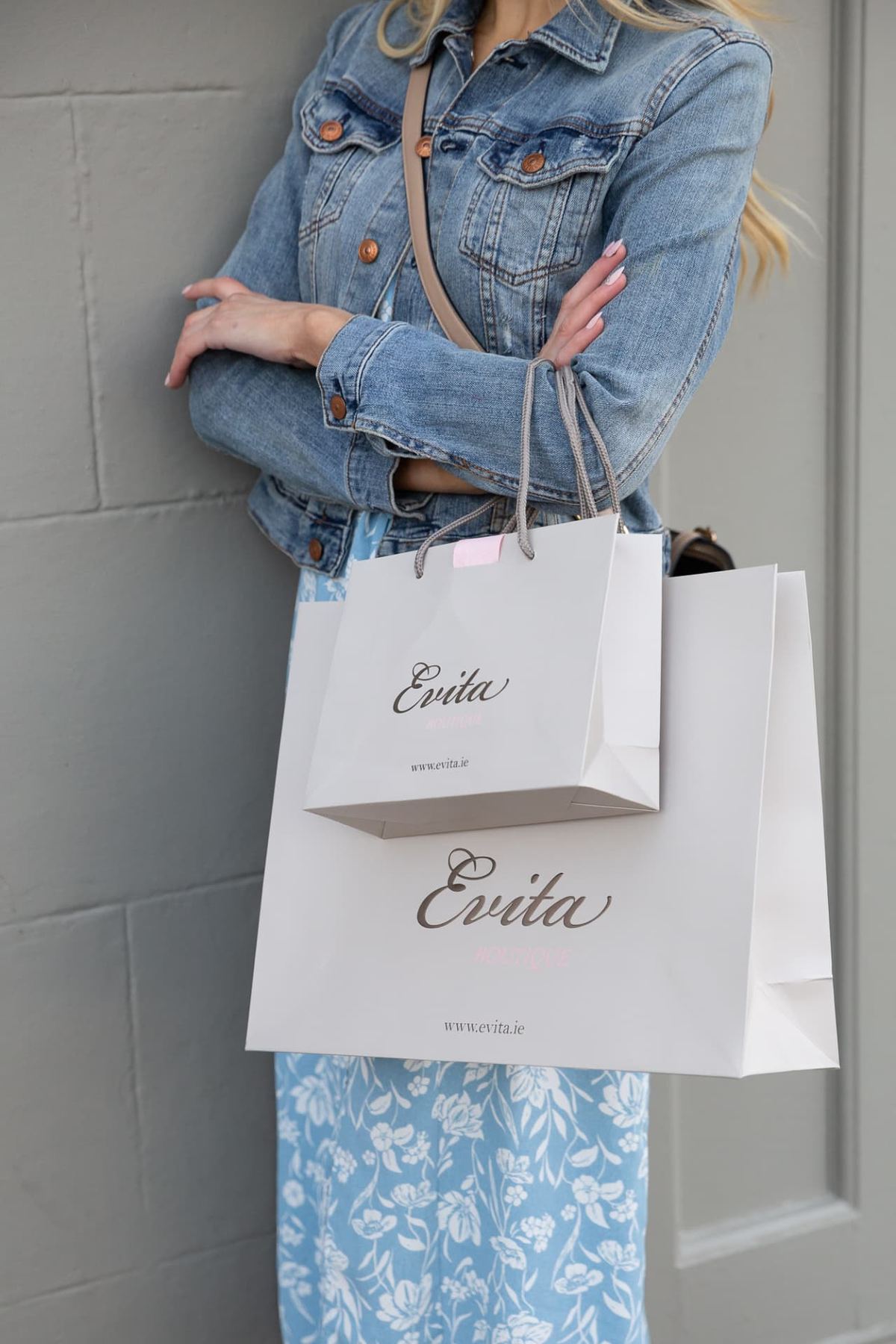 Two matt white rope handle paper bags with rose gold foil Evita logo and web address. One smaller square, one larger landscape.